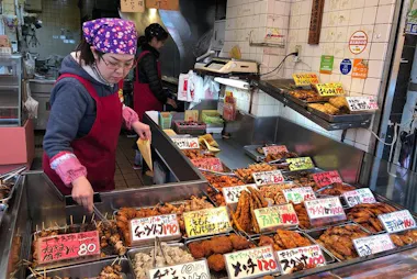 Vendor behind trays of fried food on a Jujo shopping street