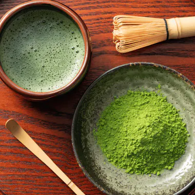 A matcha break. Bowl of whisked matcha beside matcha powder and a bamboo whisk