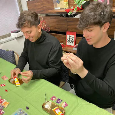 A hands-on Japanese craft workshop. Two travelers making small crafts at a workshop table