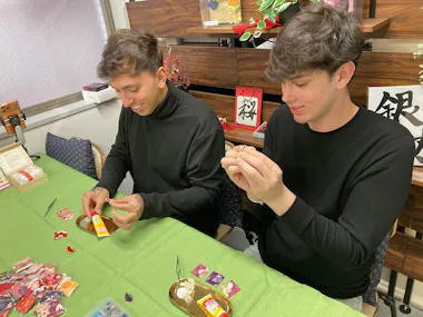 Two travelers making small crafts at a workshop table