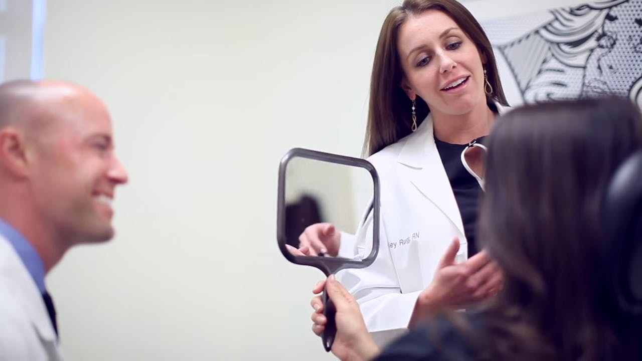 Staff speaking with a female patient while she looks in a handheld mirror