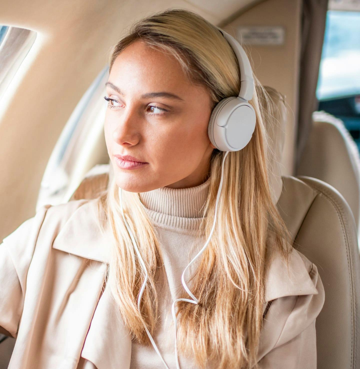 Female with blonde hair wearing headphones and a beige top & coat