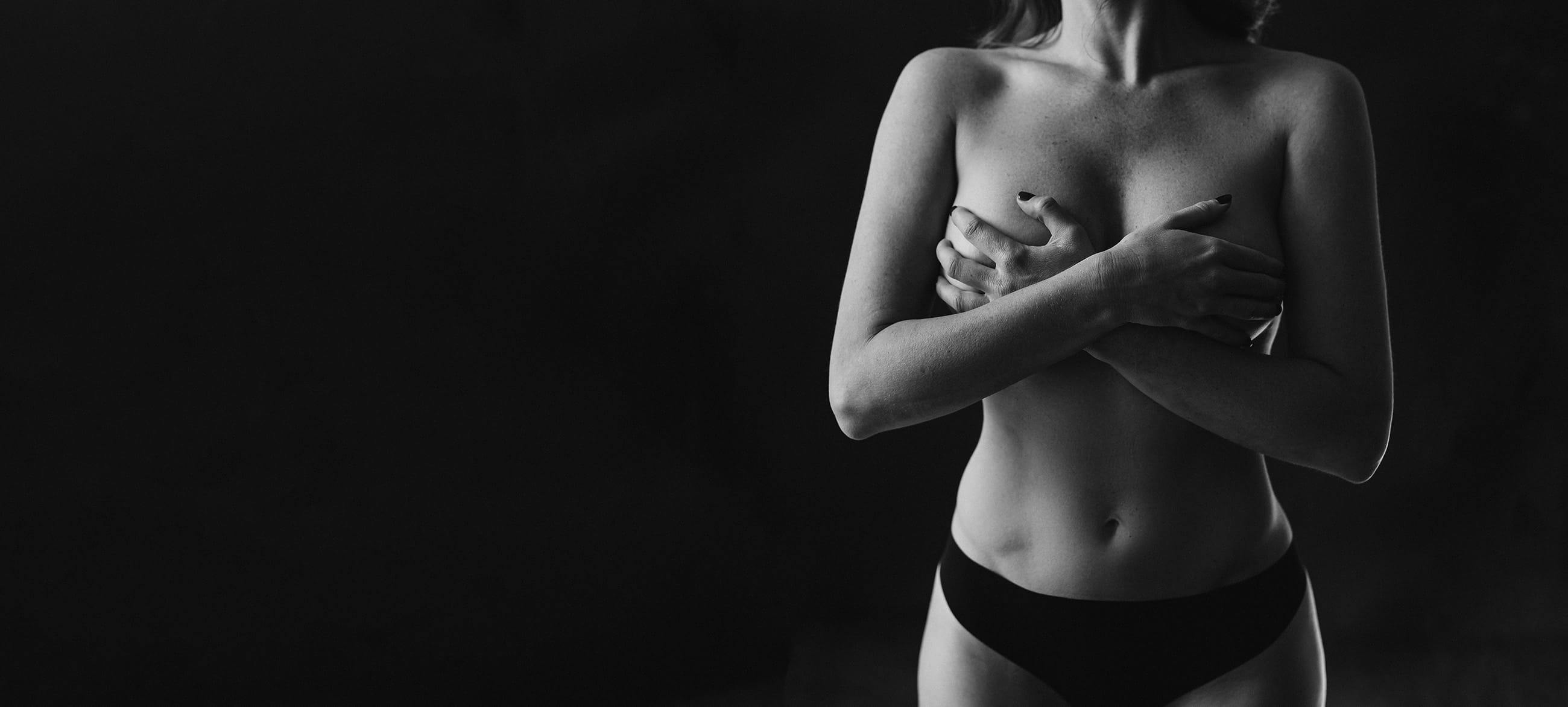 Black and white image of a topless woman covering her breasts with her hands
