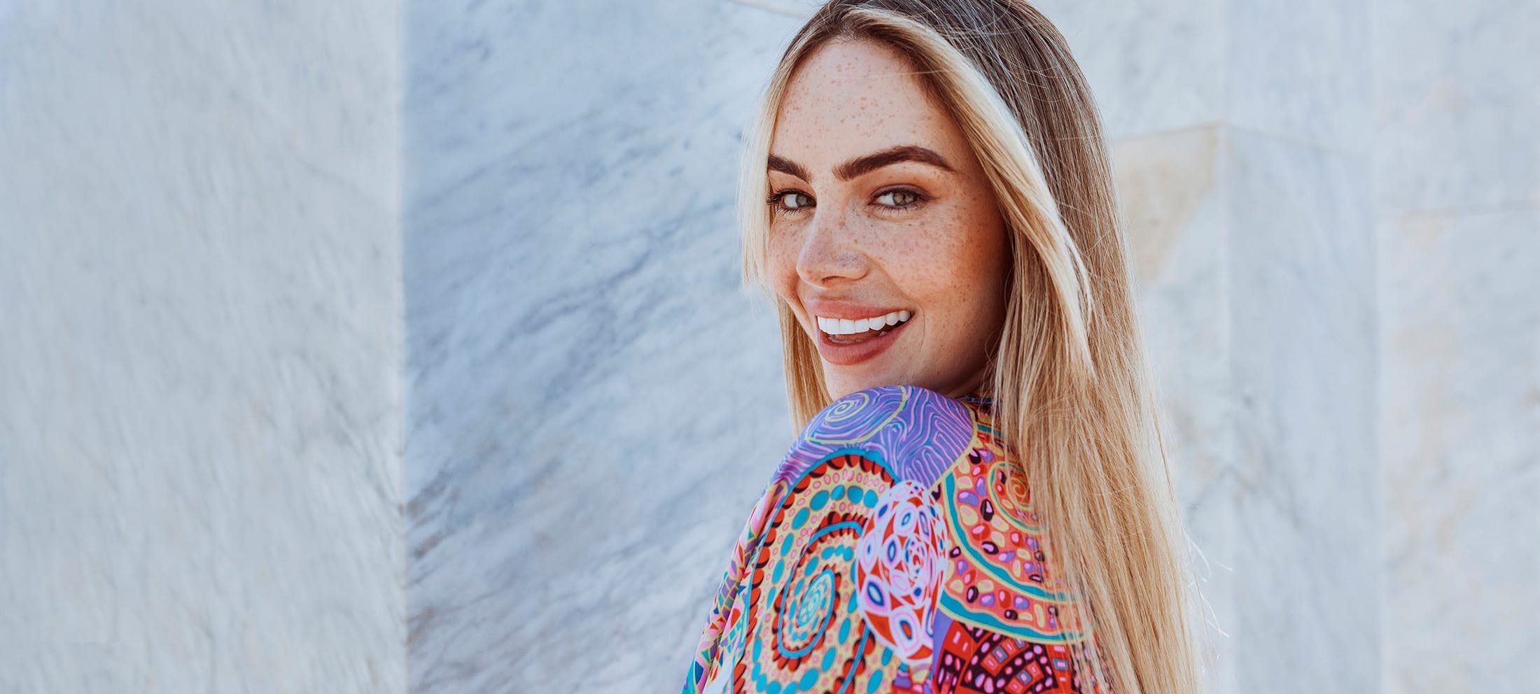 Pretty woman with blonde hair and freckles smiling and swearing a colorful top