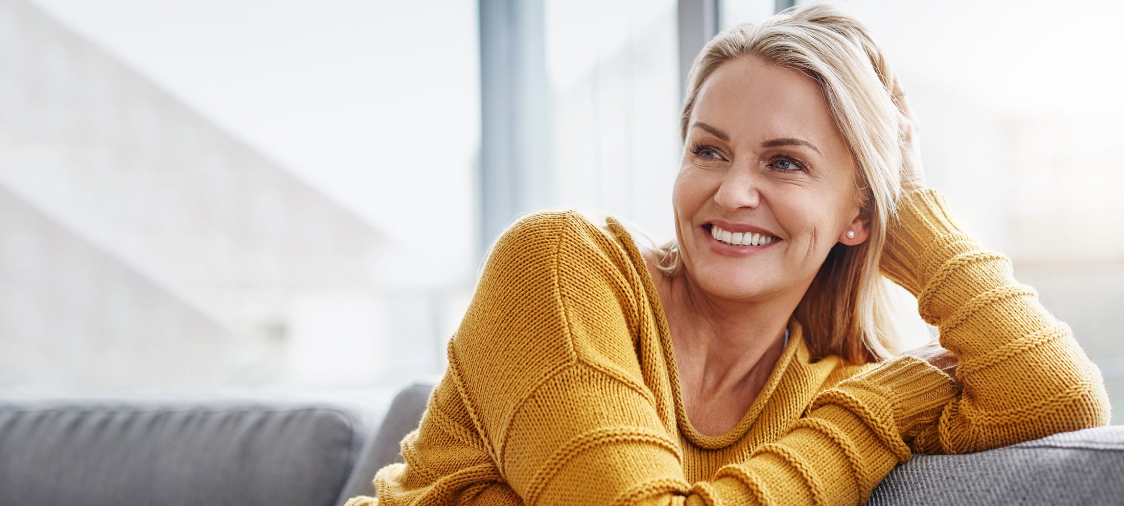 Woman in a yellow sweater sitting on a couch smiling