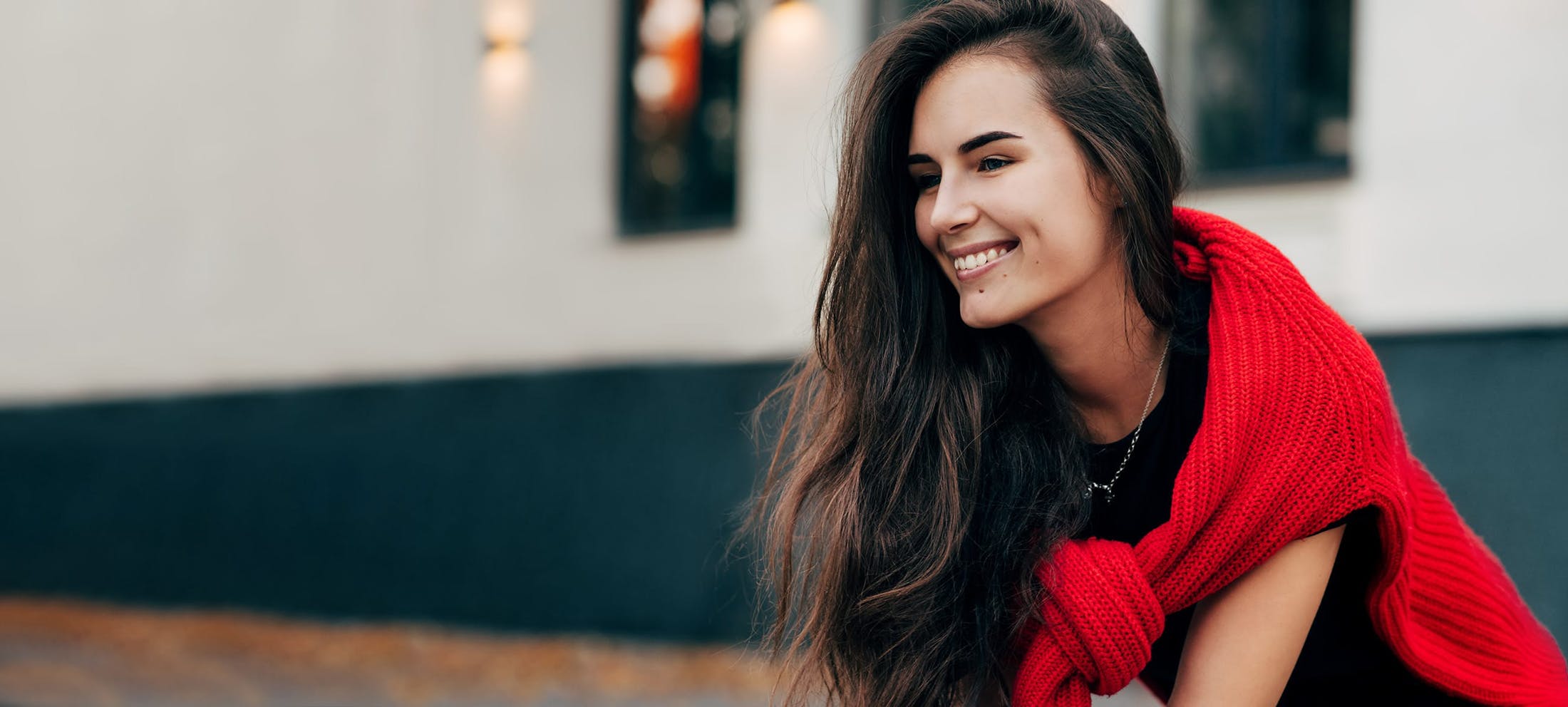 Woman with long dark hair and a red sweater around her shoulders