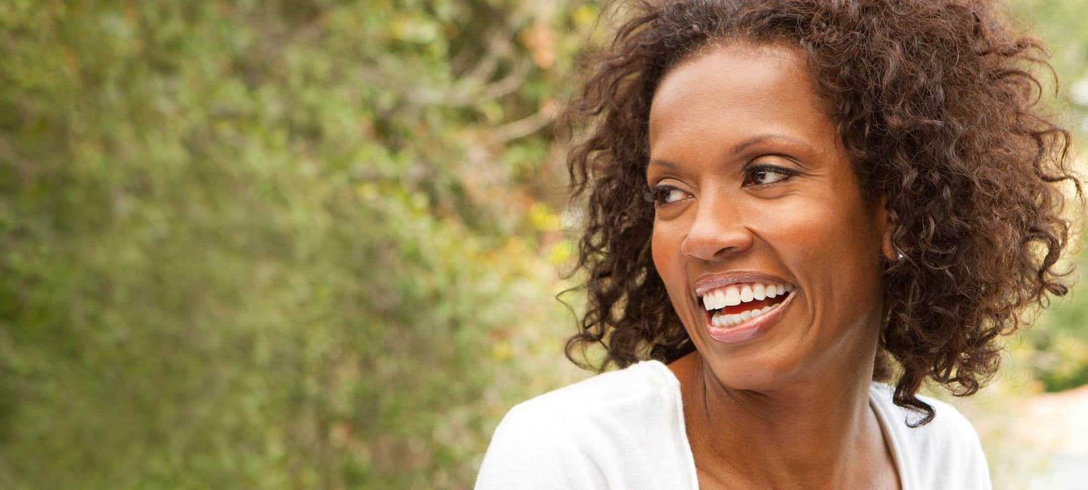 Woman with very curly hair smiling outside