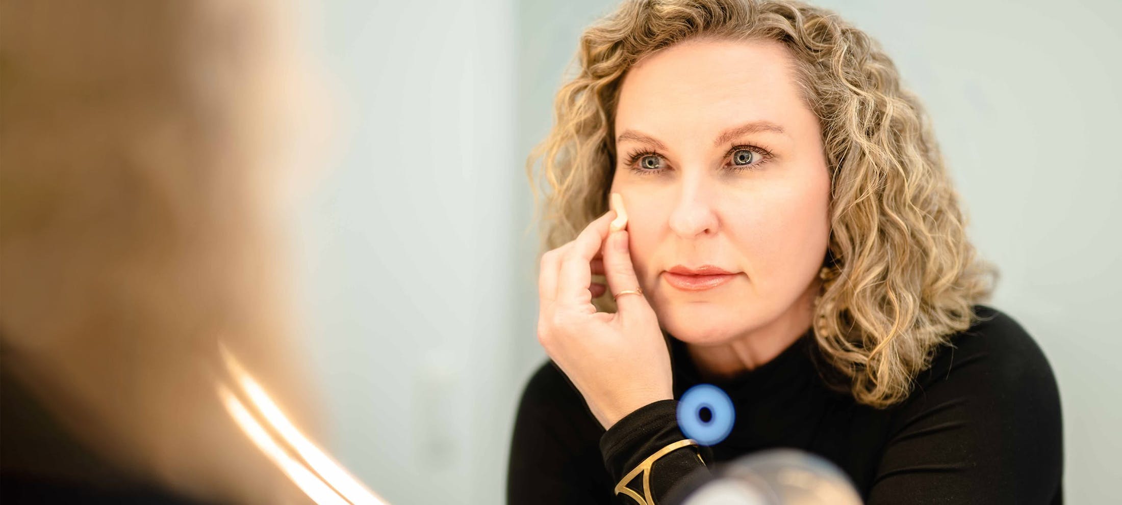 Woman with blonde curly hair looking in the mirror