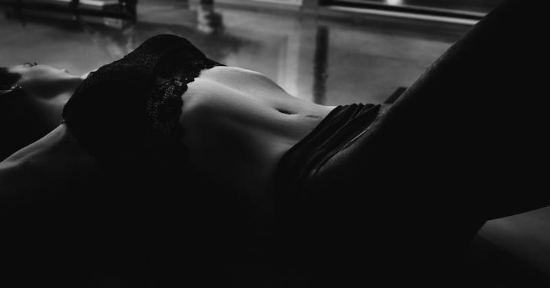 Black and white photo of a woman in lingere laying on floor