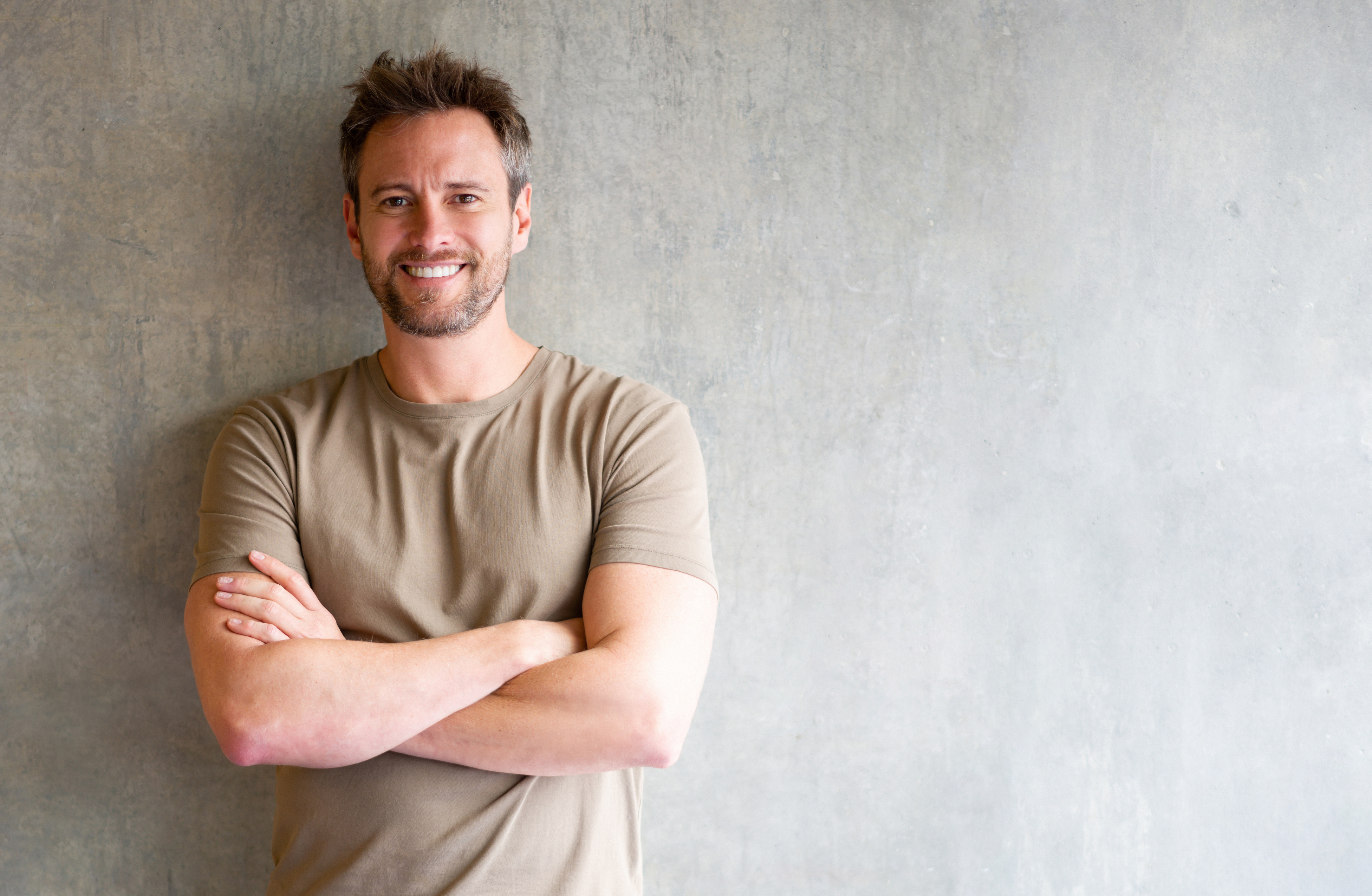 Handsome man standing in front of a grey wall crossing his arms