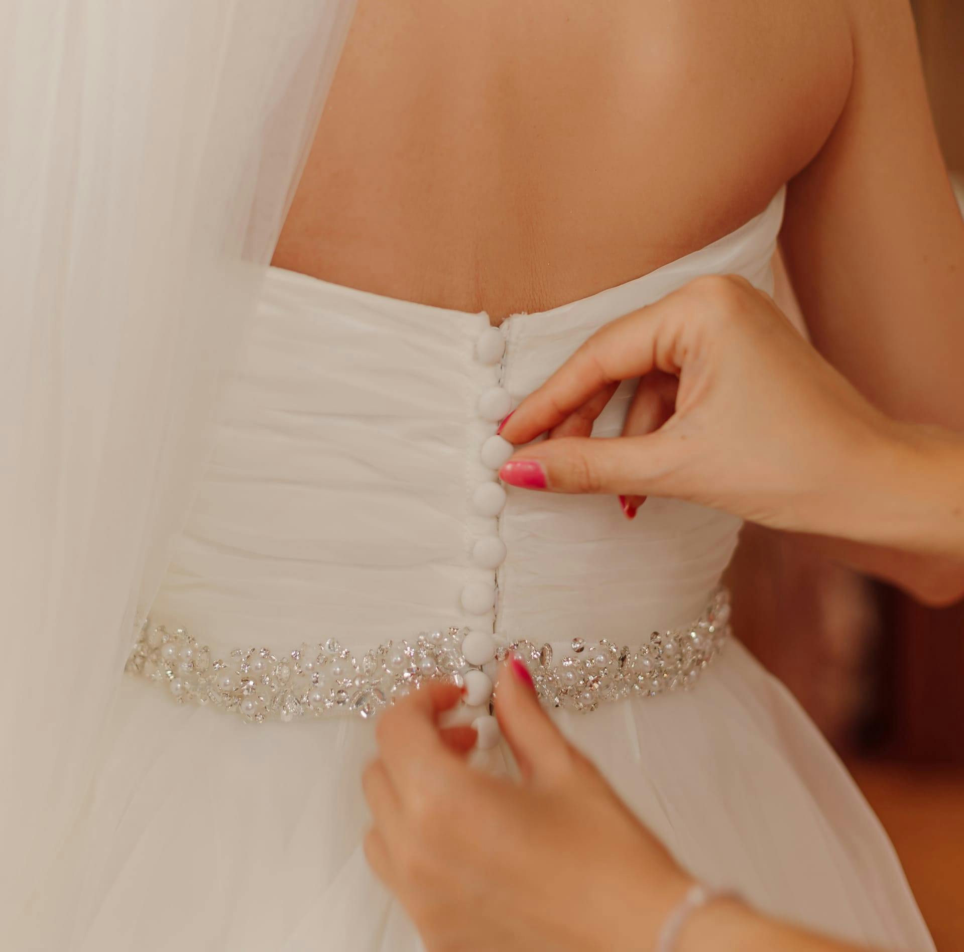 A woman buttoning up the back of a wedding dress