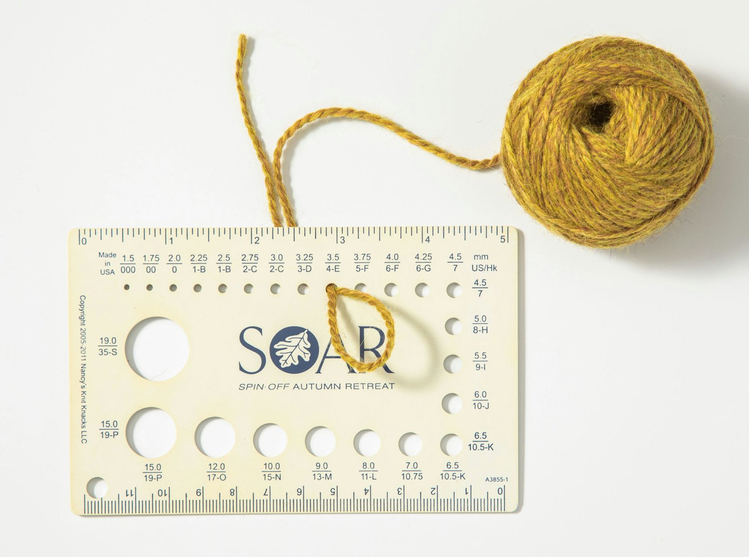 Yellow yarn with loop pulled through size 4 (3 mm) hole in knitting needle gauge