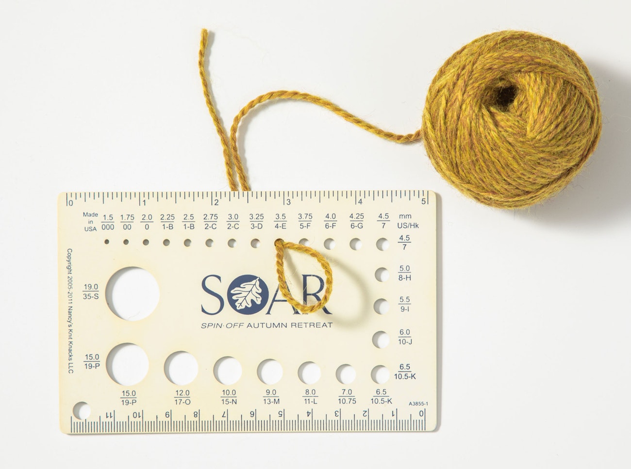 Yellow yarn with loop pulled through size 4 (3 mm) hole in knitting needle gauge