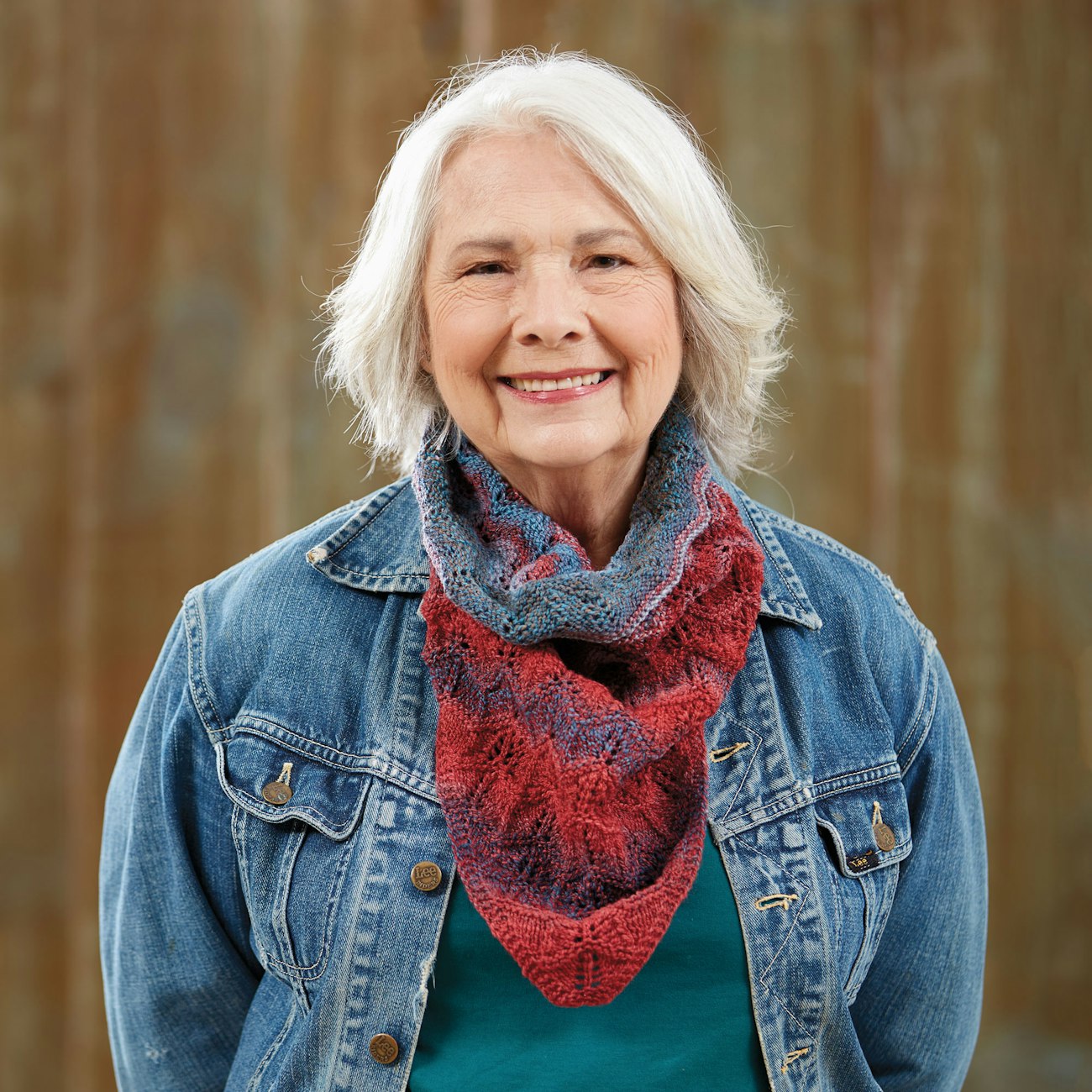 Woman with white hair wearing jean jacket and handknitted red and blue cowl.