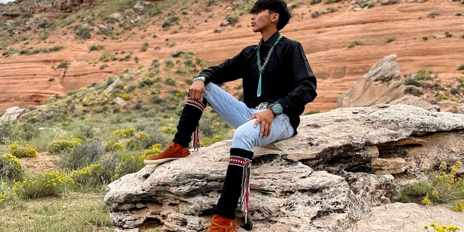 Young Diné man sitting on rock wearing black handknitted leggings