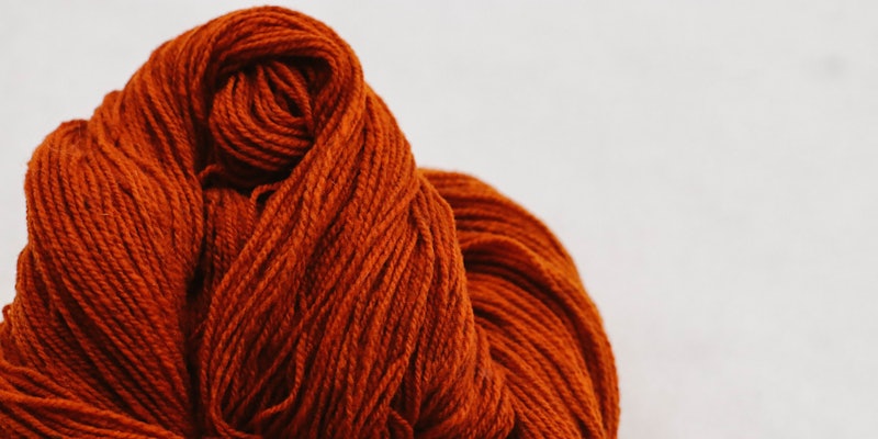 Skein of orange wool yarn on white snowy background