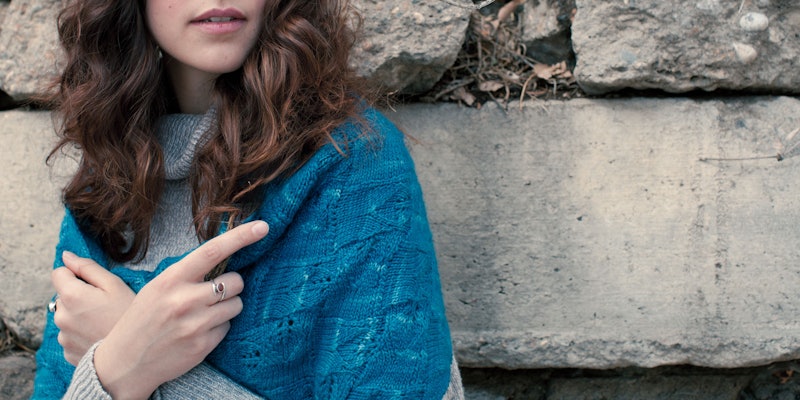 Woman with brown hair wearing teal shawl against stone wall