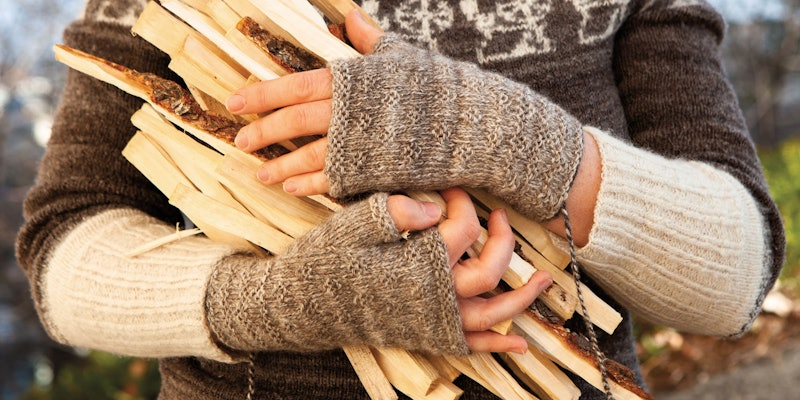 Woman in brown and white sweater, arms full of kindling, wearing fingerless knitted mitts