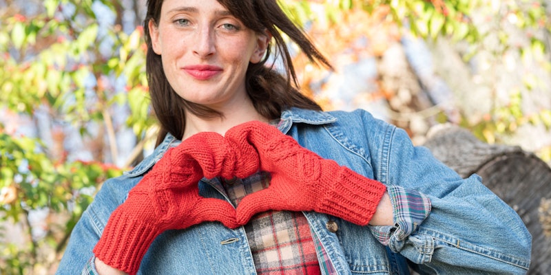 Model wearing a pair of red cabled mittens and denim jacket