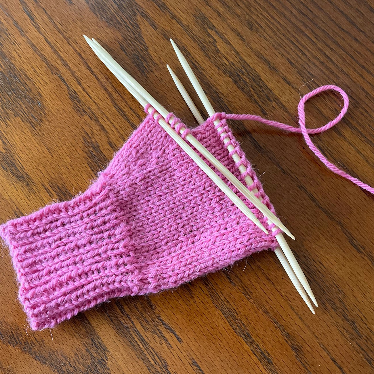 Pink mitten in process on double-pointed knitting needles