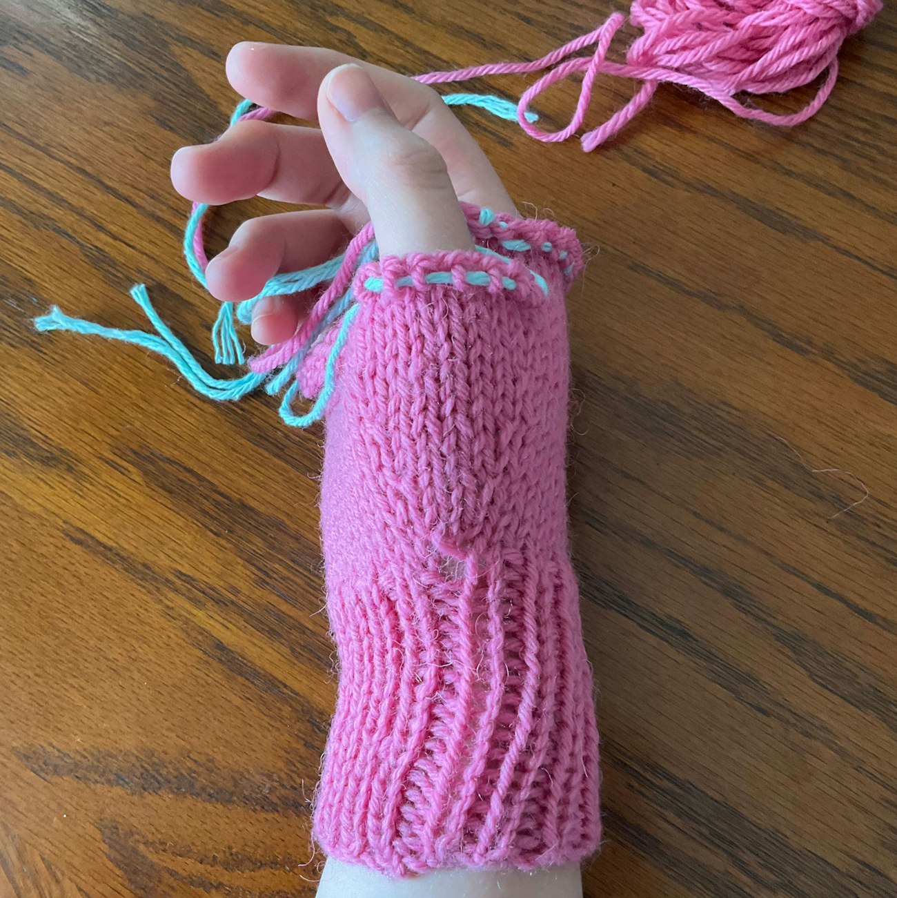 Pink mitten in process with stitches held on waste yarn