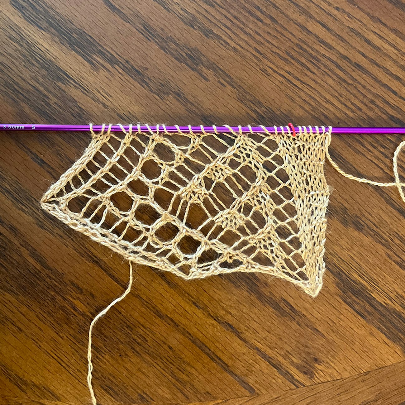 One repeat of lace knitting in gold yarn on purple needle