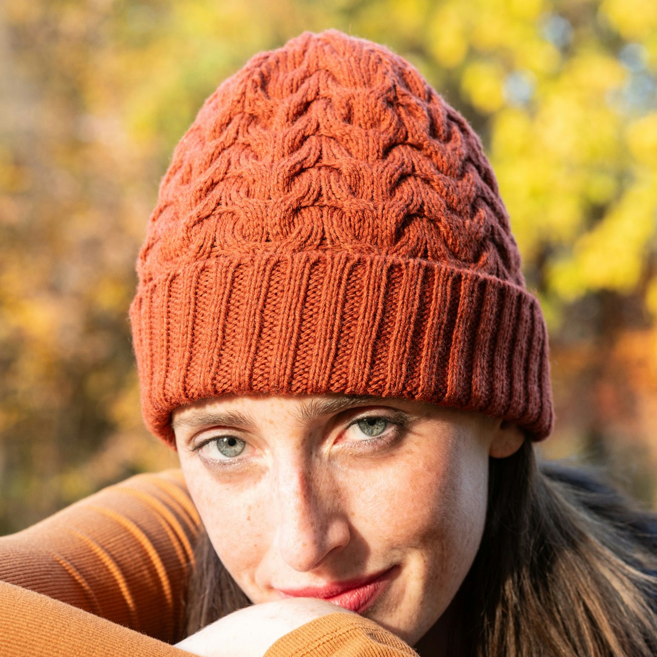Model with brown hair wears dark orange cabled toque