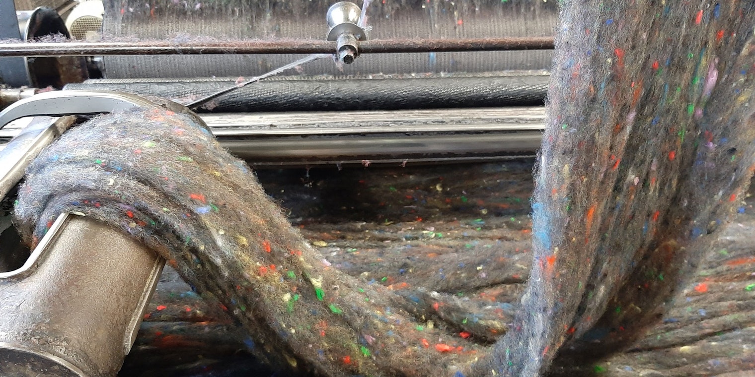 Small flecks of tweed dispersed in a web of wool roving