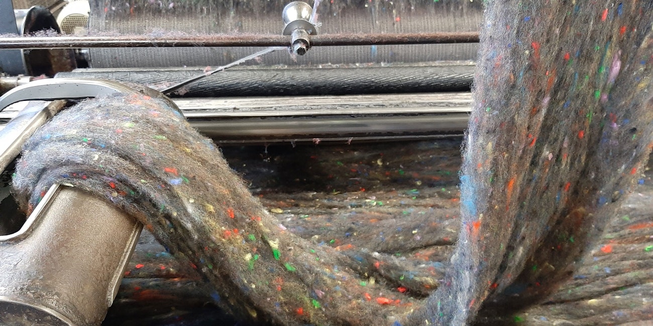 Small flecks of tweed dispersed in a web of wool roving