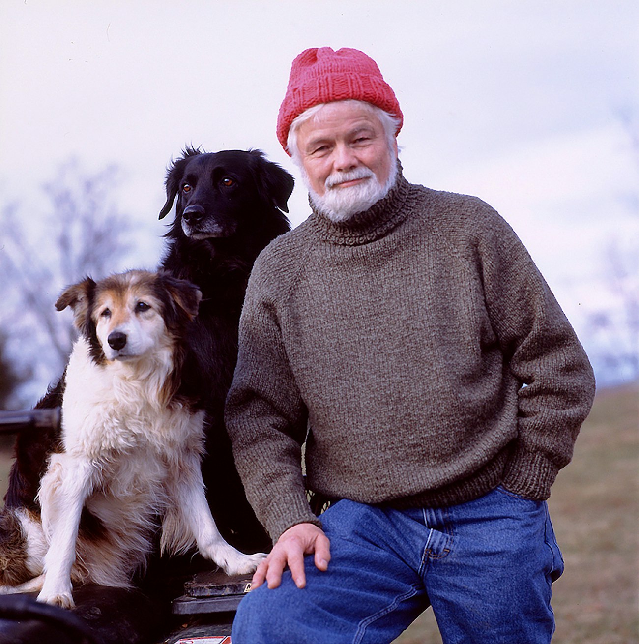 Man with white beads and red hat with 2 dogs