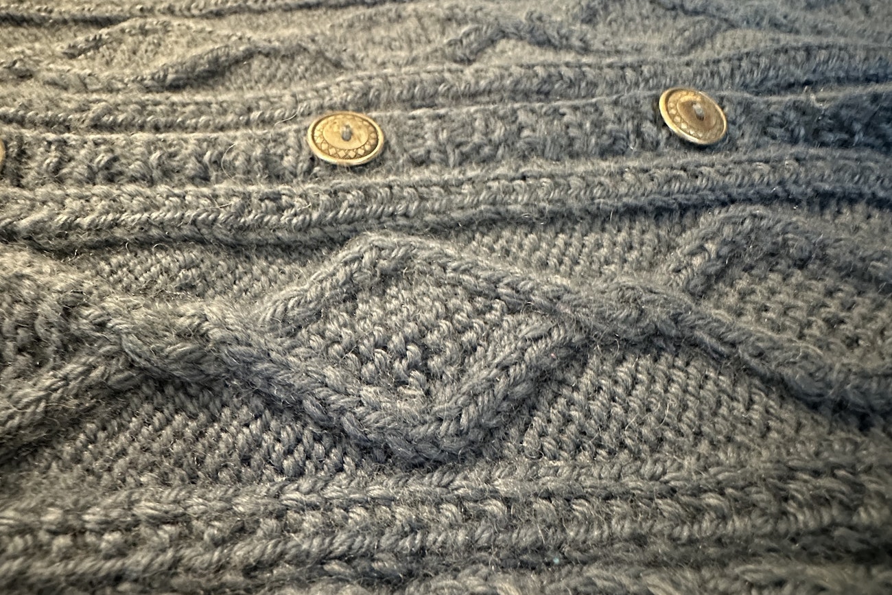 Brass buttons on the front of a gray cabled sweater
