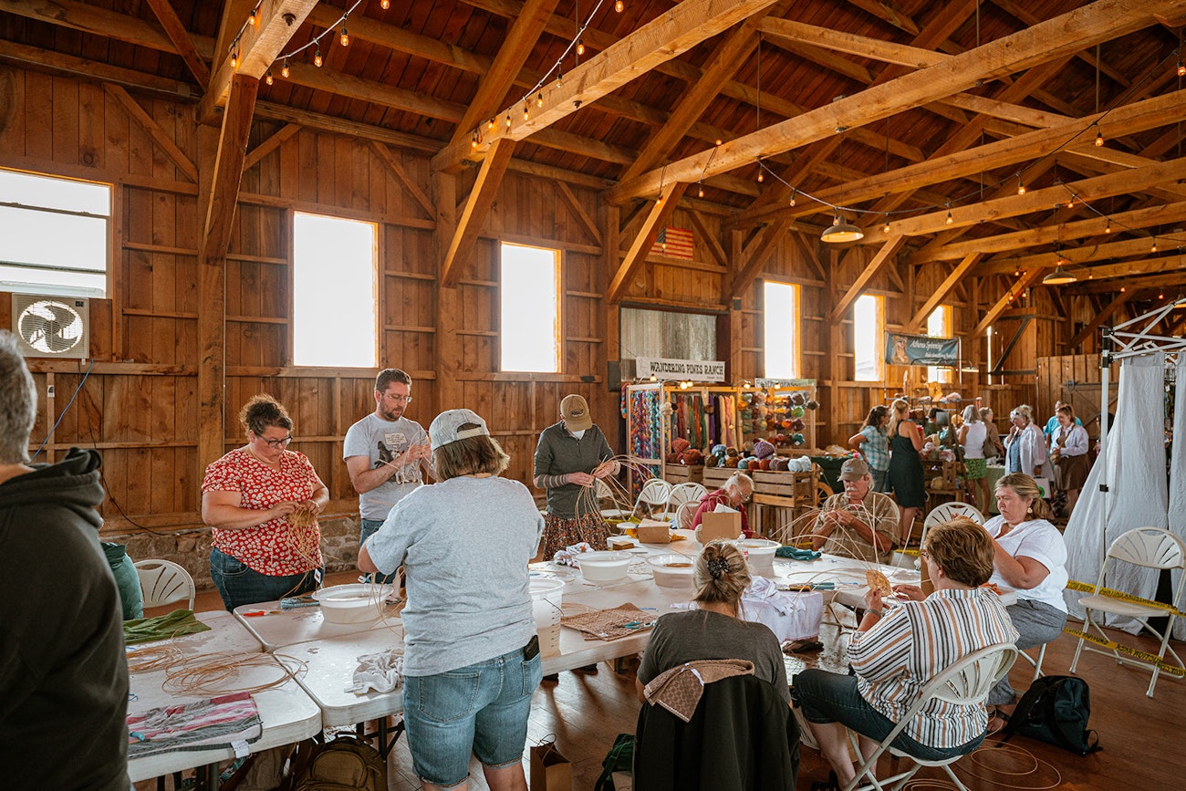 Group of people standing and sitting around a table in a high-ceiling barn