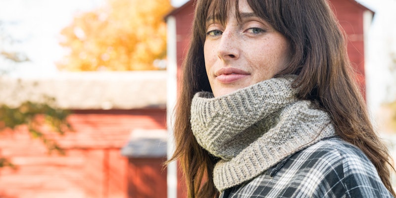 Woman with dark hair wearing a gray wool cowl, red barn in background