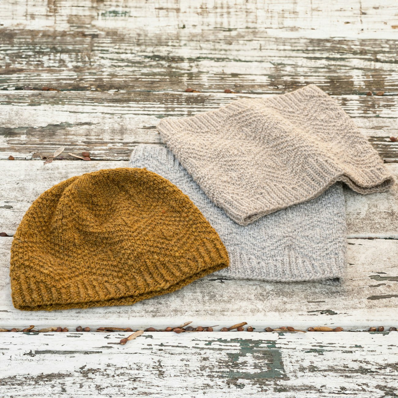 Dark gold hat, beige cowl, and gray cowl on weathered wood table