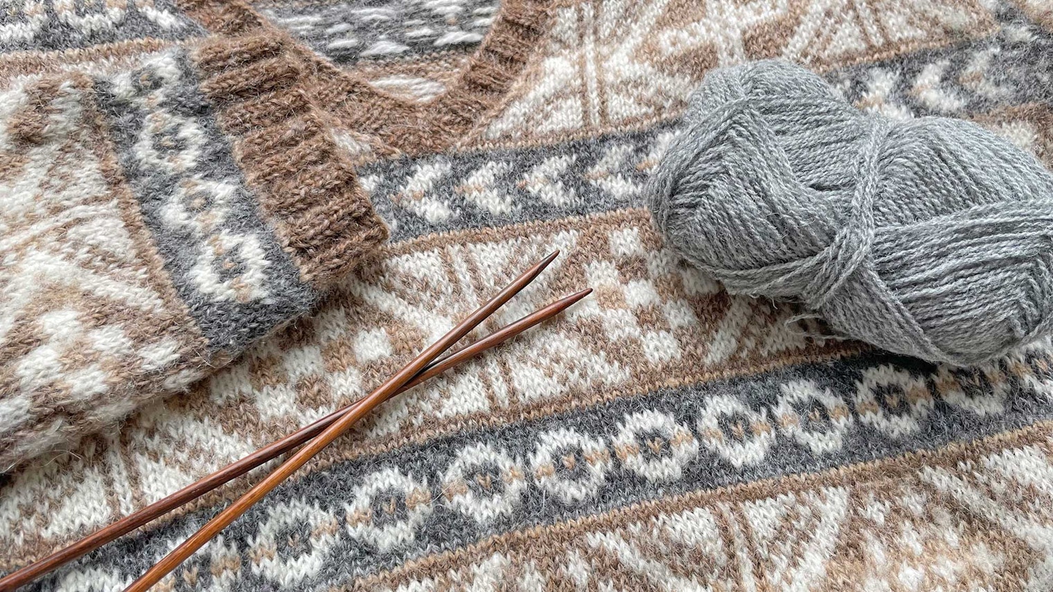 Colorwork sweater in shades of cream, brown, and gray, with yarn and needles