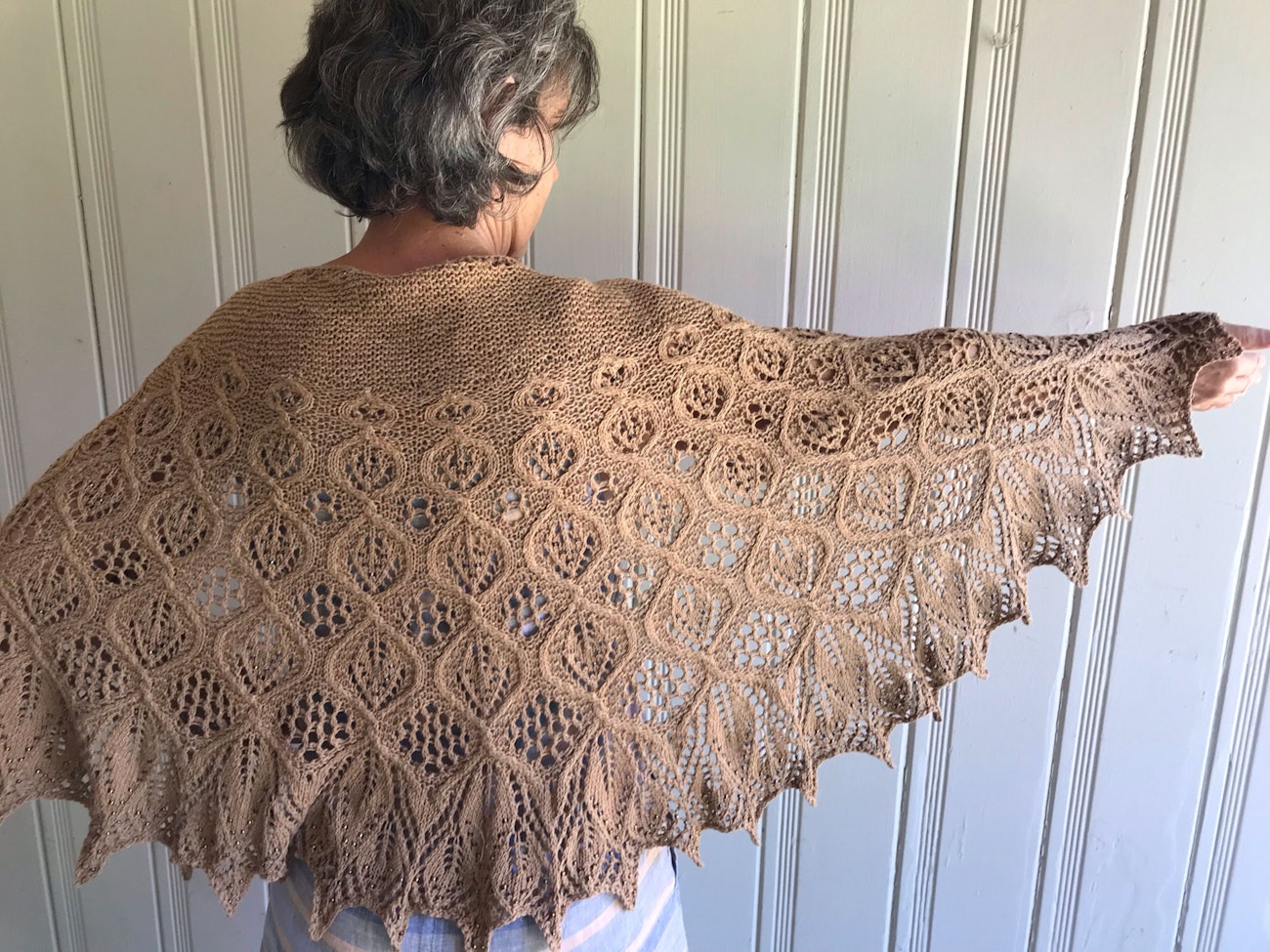 Woman facing away with arms outstretched to show brown knitted lace shawl