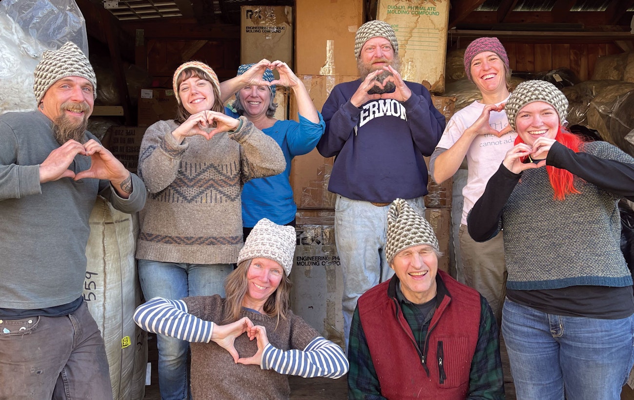 8 people of mixed ages, making heart signs with their hands, all wearing knitted hats