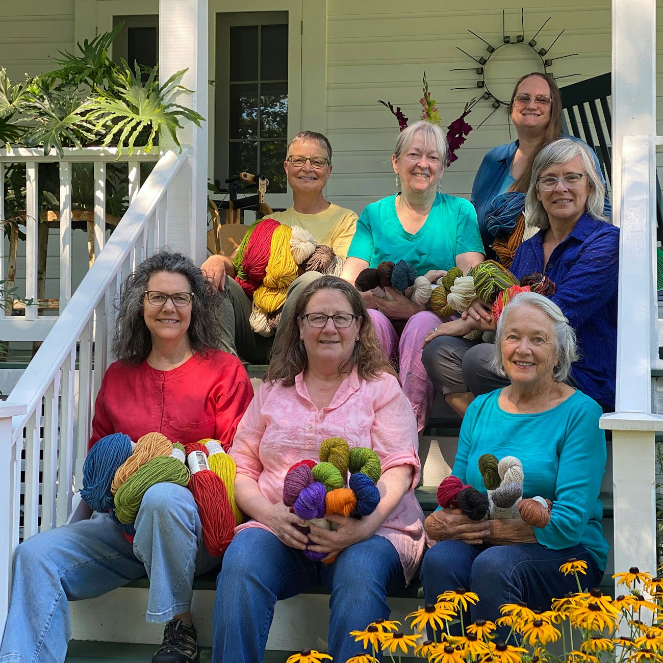 Seven women sitting on white porch steps holding yarn