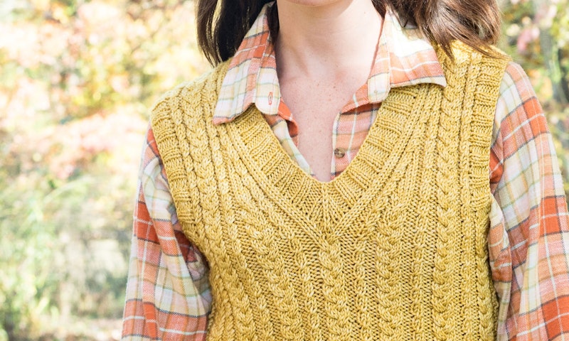 A model showcases knitted gold v-neck vest with cables