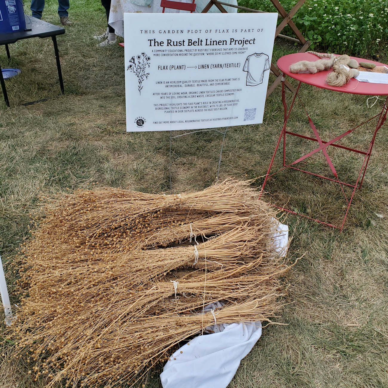 Bundles of unprocessed dried flax lying on the ground in front of a sign for the Rust Belt Linen Project