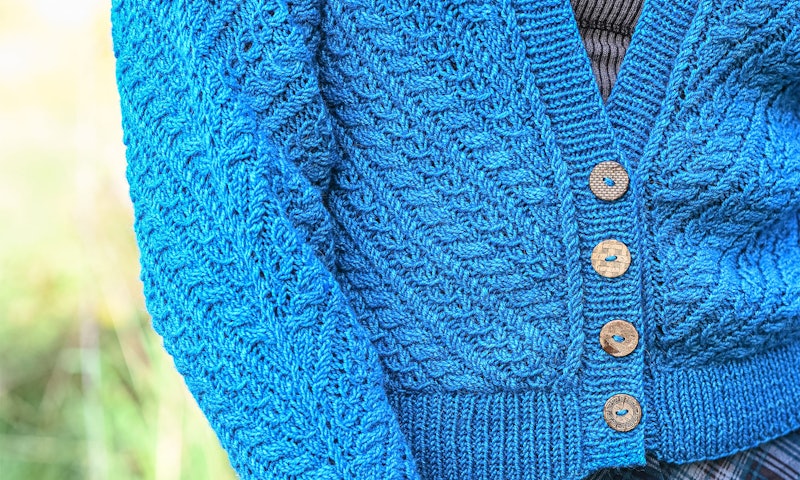 A blue handknit cabled sweater with button closures.