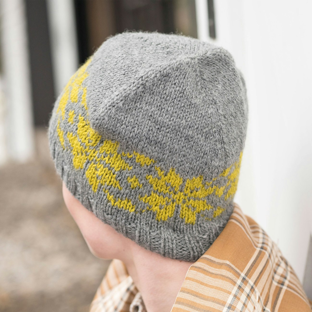 A gray and yellow colorwork handknitted cap on a young man sitting outside