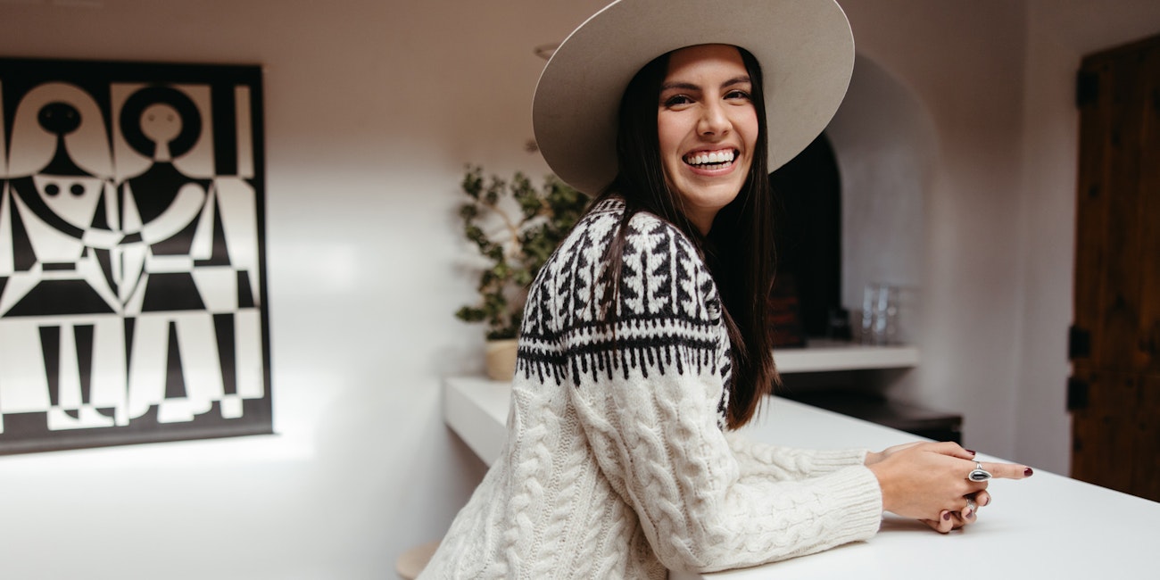 Woman in black and white sweater wearing hat leaning on counter