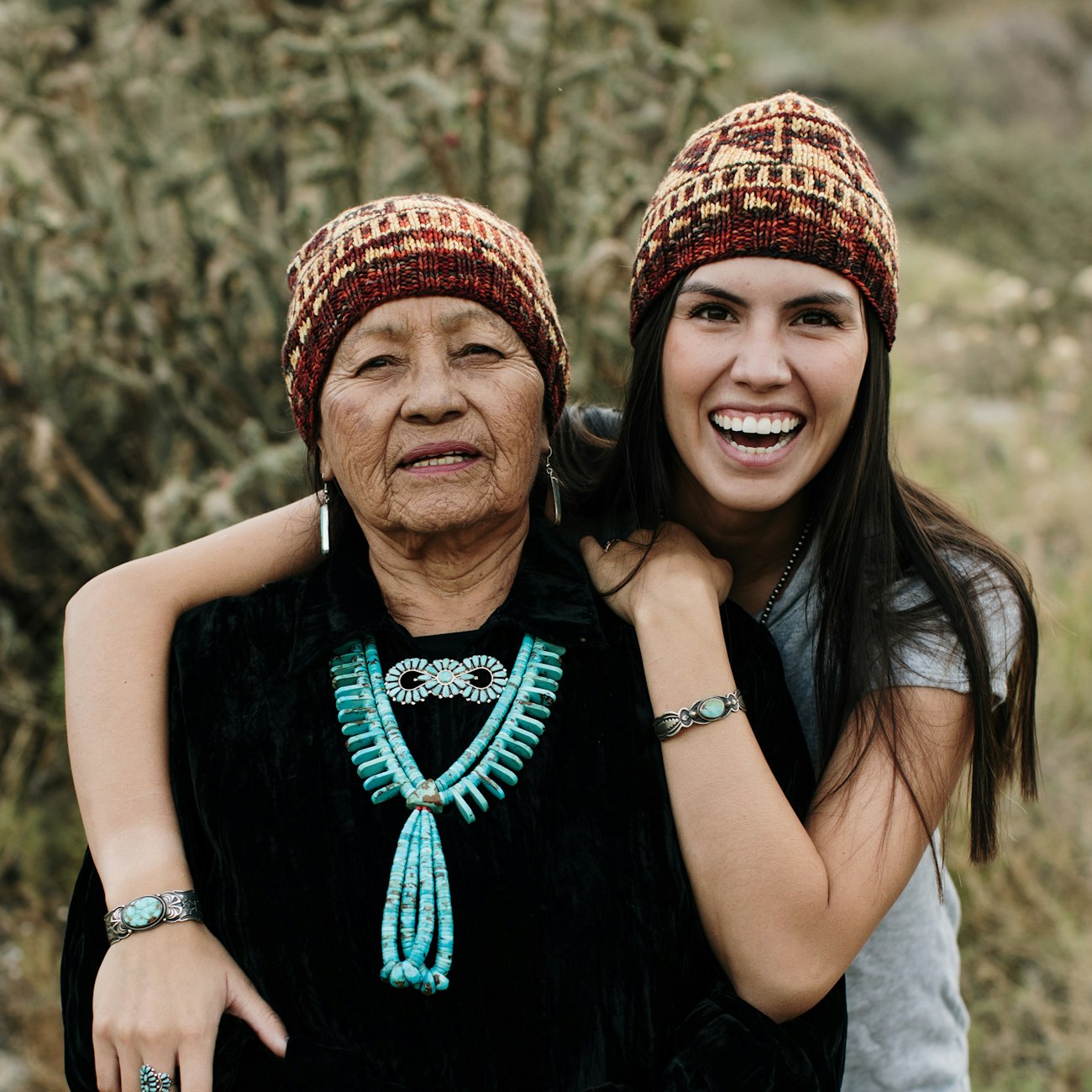 Older woman wearing turquoise and younger woman wearing identical yellow and brown knitted hats