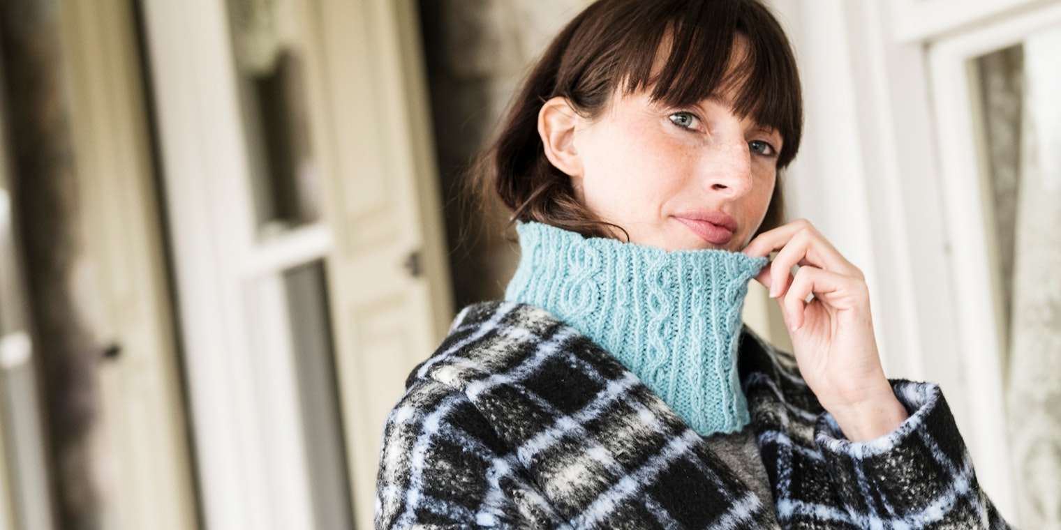 Woman with brown hair and light blue knitted cowl under plaid coat