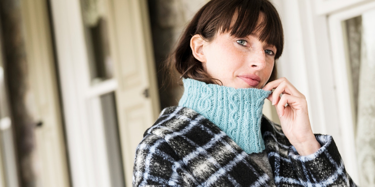 Woman with brown hair and light blue knitted cowl under plaid coat