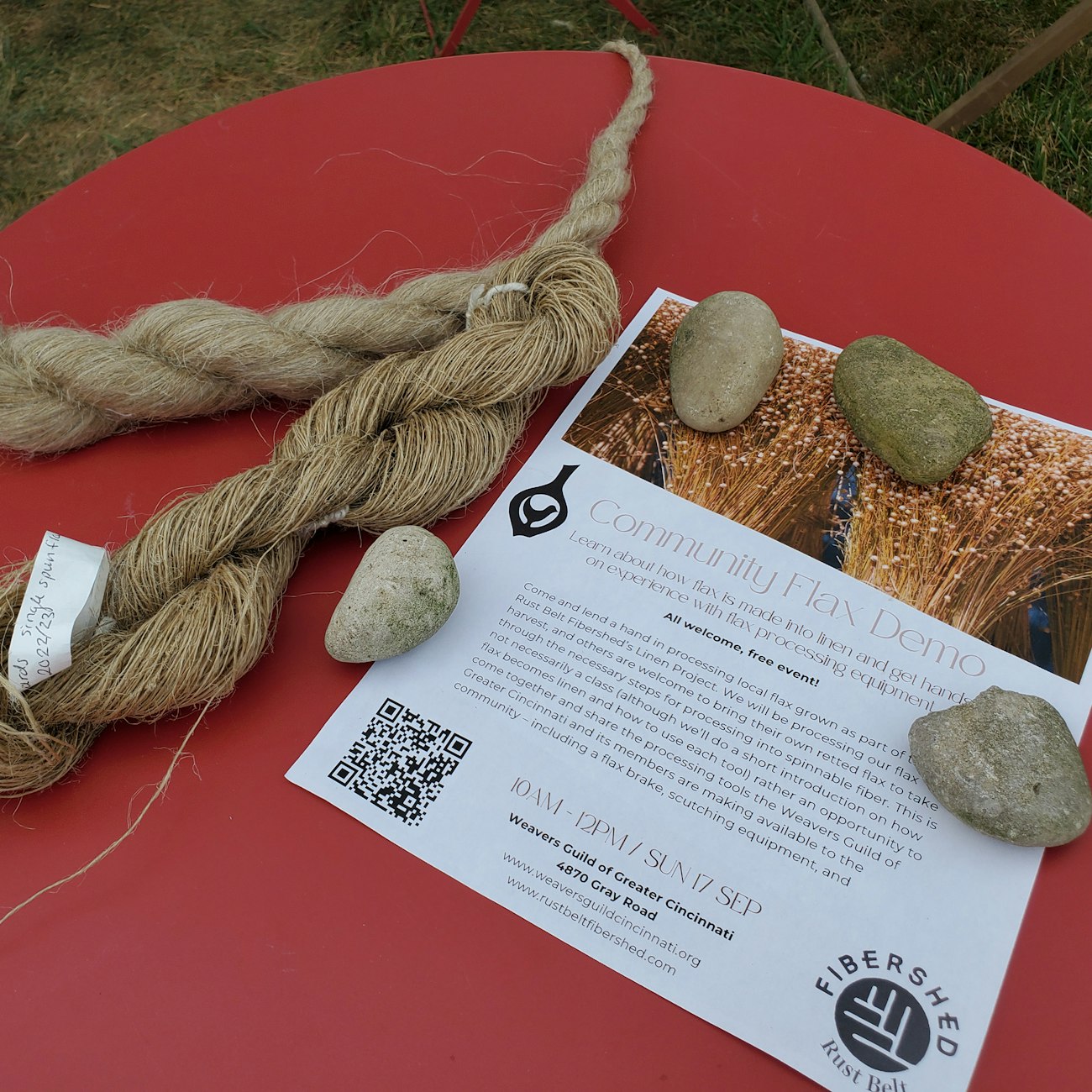 Hanks of coarse and fine flax on a red table with a flyer for a community demonstration