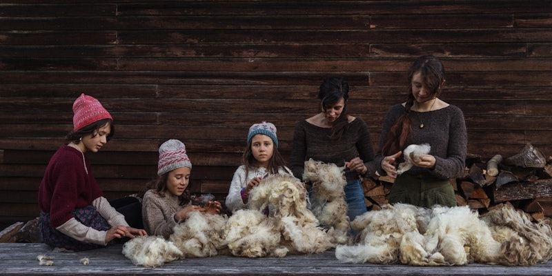 Three children in handknitted wool hats, one teenager, and one adult woman sorting raw wool