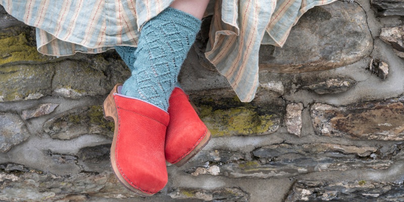 Feet in aqua socks and red clogs against stone wall