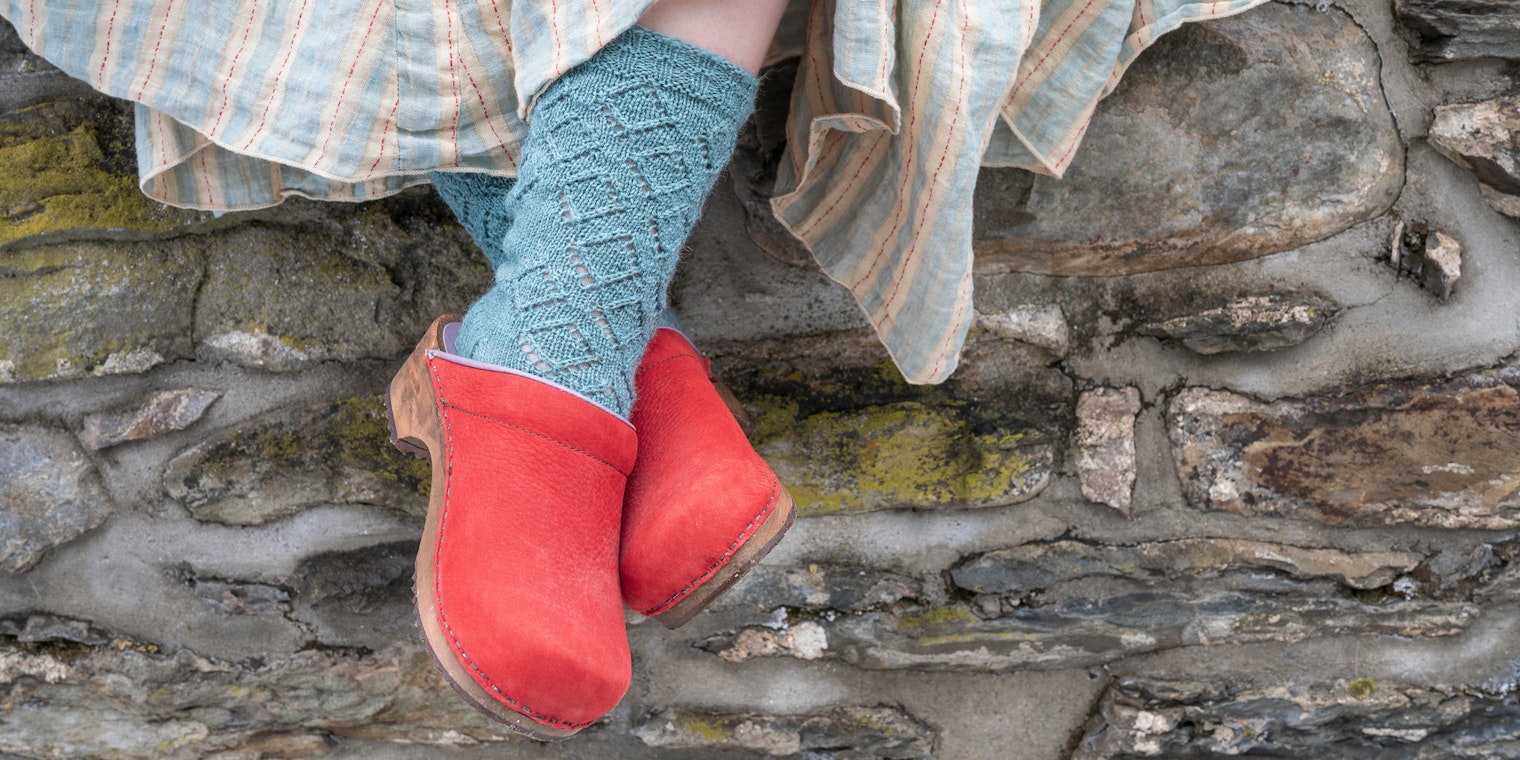 Feet in aqua socks and red clogs against stone wall
